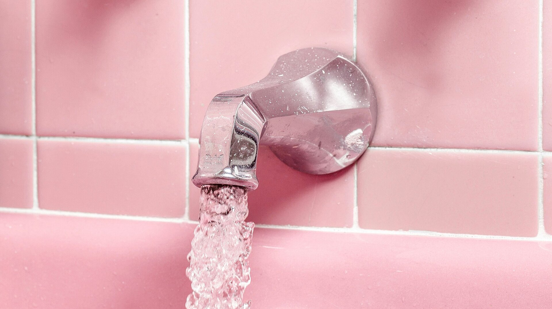 Ein Wasserhahn vor Fliesenhintergrund aus dem Wasser sprudelt