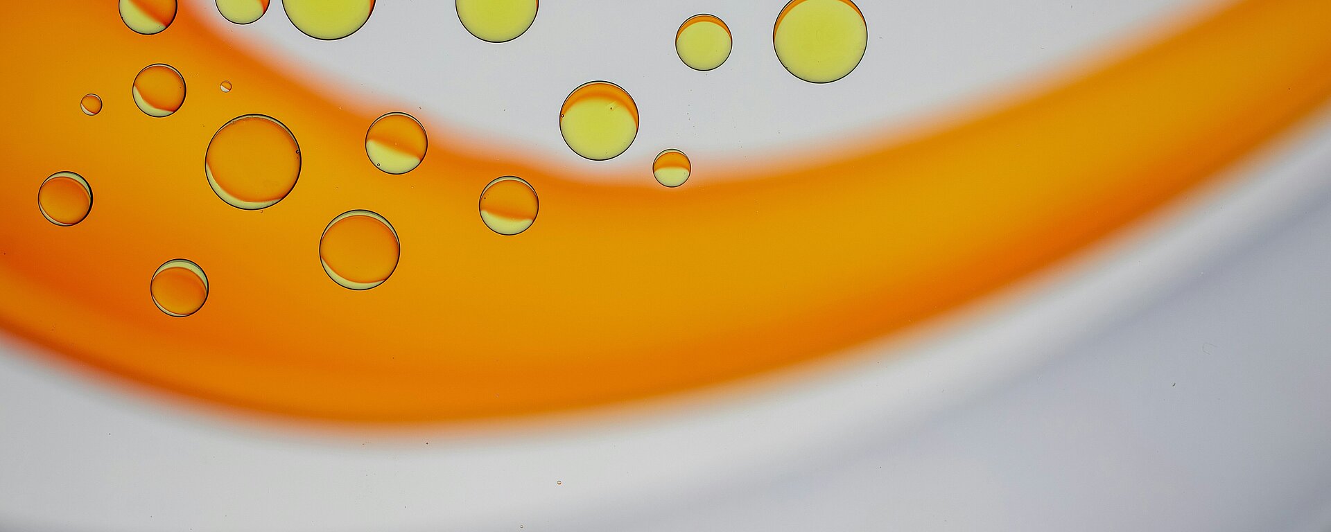 Nahaufnahme von gelben und orangefarbenen Flüssigkeitstropfen auf einer glatten Oberfläche.