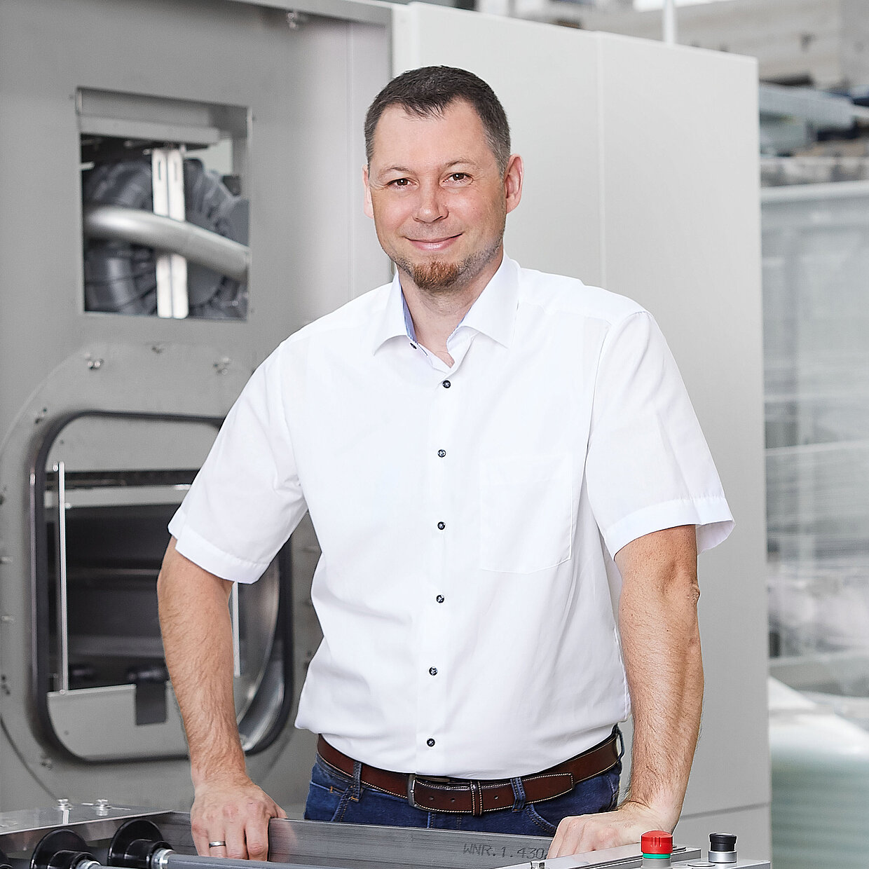 A person in a white business shirt in front of a MAFAC cleaning system. A transfer system is in the foreground.