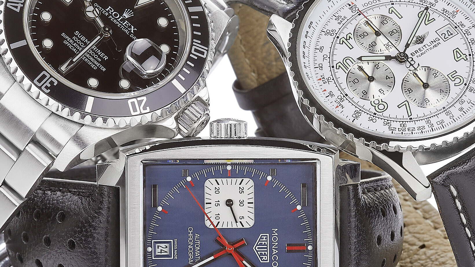 Drei Luxusuhren, darunter eine mit schwarzem Zifferblatt, eine mit blauem Zifferblatt und eine mit weißem Zifferblatt, auf weißem Hintergrund.