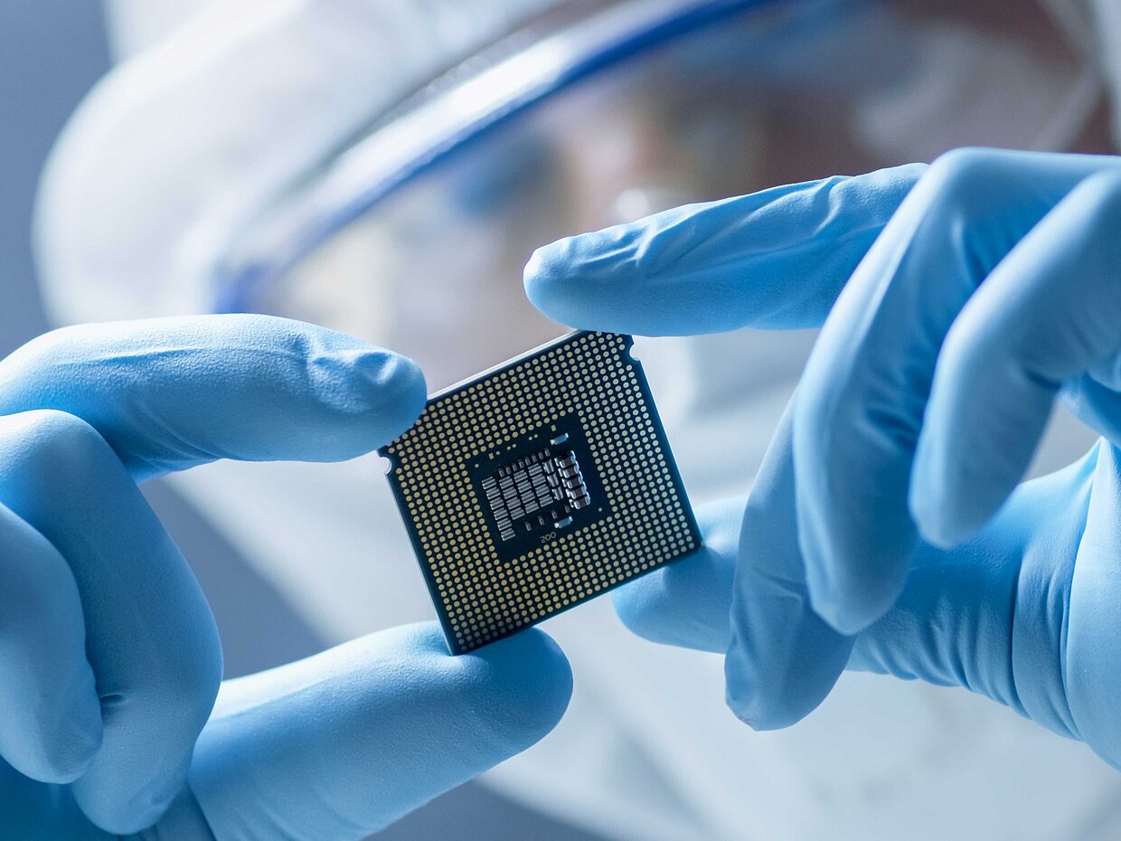 Nahaufnahme einer Person, die Reinraumkleidung trägt und einen Computerchip betrachtet