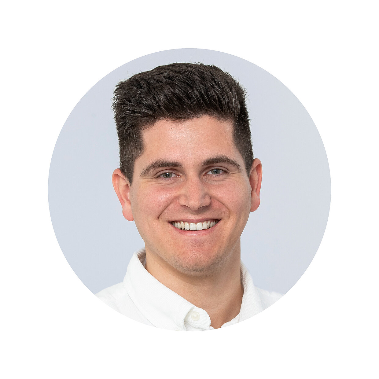 Kontaktbild Lukas Baier Porträt eines lächelnden Mannes mit kurzen dunklen Haaren in einem weißen Hemd vor einem neutralen Hintergrund.
